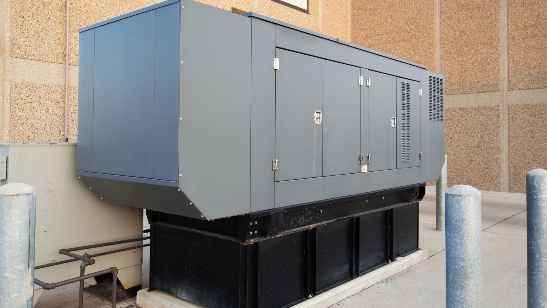 Large industrial generator with gray metal enclosure next to concrete wall